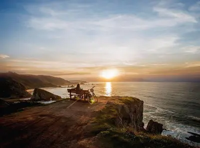 a person sitting on a bench next to the ocean at Apartamento Piscina 2G by Urraca Suites Viveiro in Viveiro