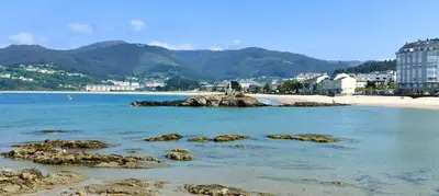 a beach with rocks in the water and buildings at Alojamientos Viveiro - Playa de Covas I in Viveiro