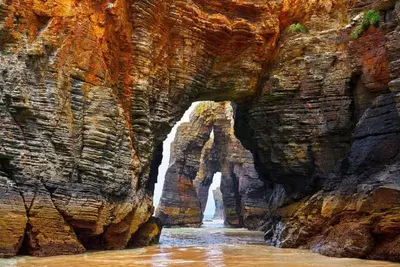 a cave in a rocky mountain with a waterfall at EnFOZ Las Catedrales: Playa, Piscina y Parking in Foz