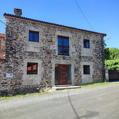a stone building with a brown door and windows at O Lar da Crega in O Pino