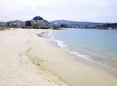 a sandy beach with buildings and the ocean at EnSAN CIPRIAN Playas y Gastronomía in San Ciprián