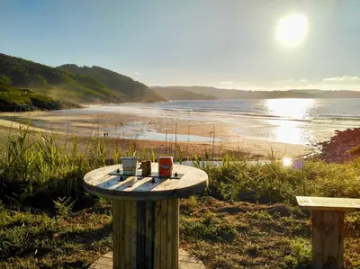 a table with two coffee mugs on it next to a beach at The Cliffs - AT Seiramar in Viveiro