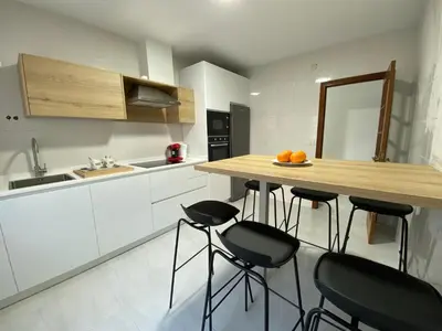 a kitchen with white cabinets and a wooden counter with stools at A tres Pasos in Caldas de Reis